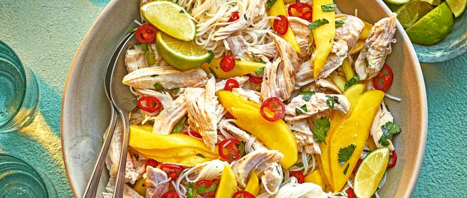 A large bowl of Chicken, mango and noodle salad with a wedge of lime and a spoon
