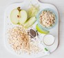 A chopping board with an apple, oats and a bowl of baby Bircher