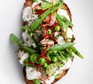 Burrata bruschetta dressed with beans and radishes, on a white surface