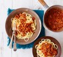 Two bowls of spaghetti topped with bolognese sauce and a pan of extra sauce on the side.